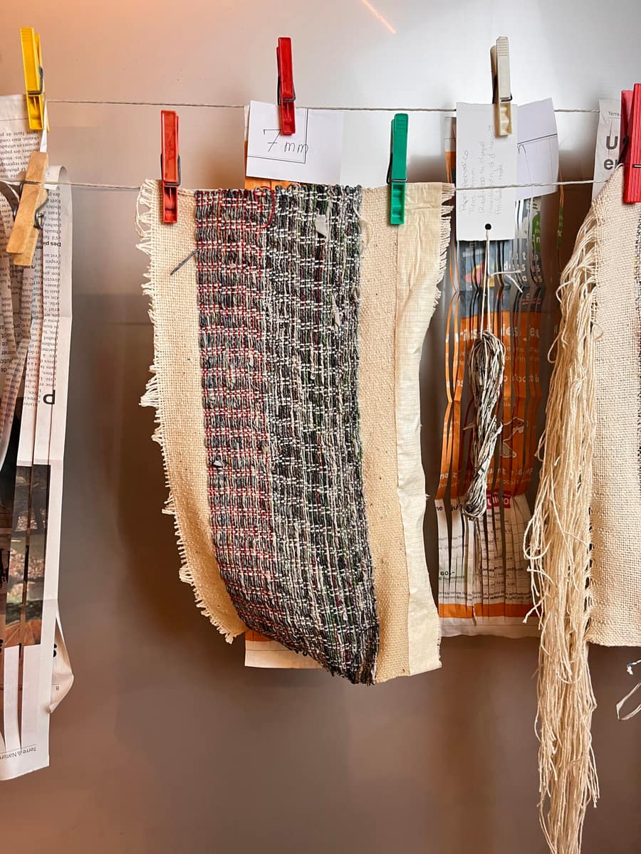 Échantillons textiles suspendus à un fil avec pinces à linge colorées, dont des pièces tissées en papier journal et fibres brutes